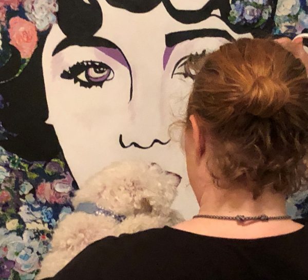 Erin from the back holding a dog and looking at a portrait of a woman